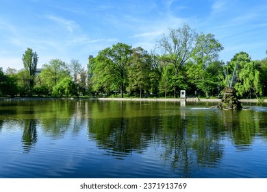Vivid green landscape with old large linden trees and small boats near the lake in Cismigiu Garden (Gradina Cismigiu), a public park in the city center of Bucharest, Romania, in a sunny spring day - Shutterstock ID 2371913769