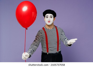 Vivid happy young mime man with white face mask in striped shirt beret hold give present colorful air inflated helium balloon to you isolated on plain pastel light violet background studio portrait