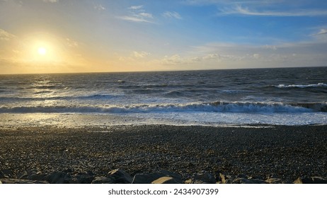 Vivid hues paint the sky as the sun dips below the horizon, casting a warm glow over the tranquil rocky beach. Sunrise brings a burst of colour, igniting the sky with hues of orange, pink, and gold.  - Powered by Shutterstock