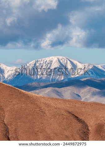 Vivid multicolored nature background of colorful highland valley among big rocky mountains. Snow surface of giant red mountain rough wall and green valley. Red orange yellow rocks. Vertical view.