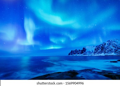Vivid Northern lights during polar night on Lofoten Islands in Norway. Epic scene of dancing aurora borealis in the night sky over jagged mountain ridge and Arctic ocean on island Senja, polar circle.