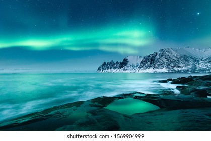 Vivid Northern Lights During Polar Night On Lofoten Islands In Norway. Epic Scene Of Dancing Aurora Borealis In The Night Sky Over Jagged Mountain Ridge And Arctic Ocean On Island Senja, Polar Circle.