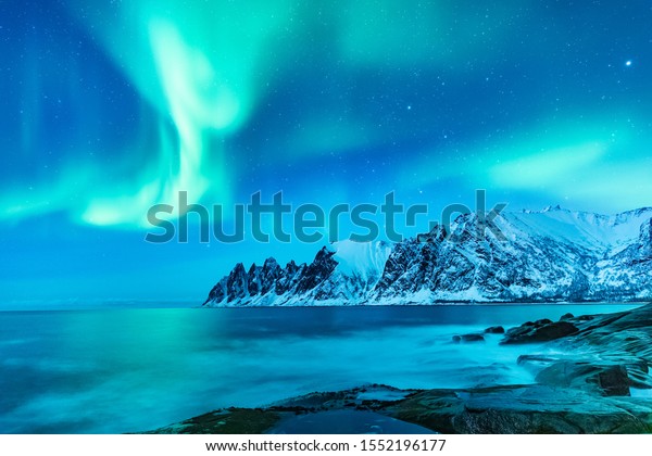 Vivid Northern lights during polar night on\
Lofoten Islands in Norway. Epic scene of dancing aurora borealis in\
the night sky over jagged mountain ridge and Arctic ocean on island\
Senja, polar circle.