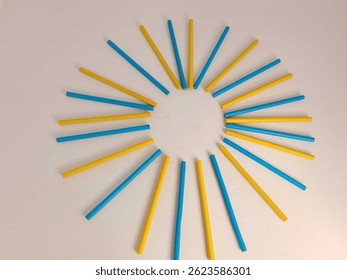 Vivid red and blue, yellow, green colored sticks are artistically placed in a circular pattern on a white background, creating a modern abstract design rich with color and symmetry.