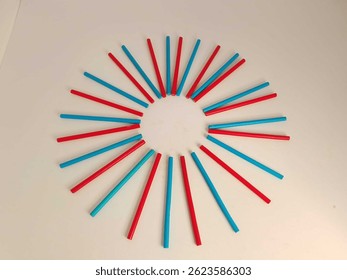 Vivid red and blue, yellow, green colored sticks are artistically placed in a circular pattern on a white background, creating a modern abstract design rich with color and symmetry.