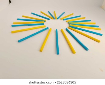 Vivid red and blue, yellow, green colored sticks are artistically placed in a circular pattern on a white background, creating a modern abstract design rich with color and symmetry.