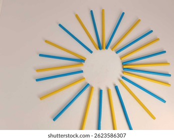 Vivid red and blue, yellow, green colored sticks are artistically placed in a circular pattern on a white background, creating a modern abstract design rich with color and symmetry.