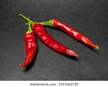 Vivid red chili peppers with green stems displayed against a contrasting dark backdrop. Fresh produce captured in high detail, perfect for themes of cooking, spicy flavors, and culinary ingredients. - Powered by Shutterstock