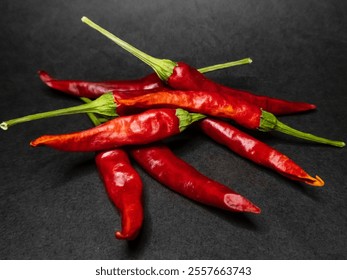 Vivid red chili peppers with green stems displayed against a contrasting dark backdrop. Fresh produce captured in high detail, perfect for themes of cooking, spicy flavors, and culinary ingredients. - Powered by Shutterstock