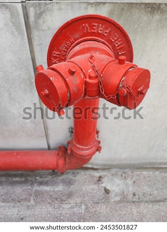 vivid red fire hydrant affixed to a grey concrete wall. The hydrant, showing signs of wear and tear, is marked with embossed text that is not visible due to the angle of the shot.