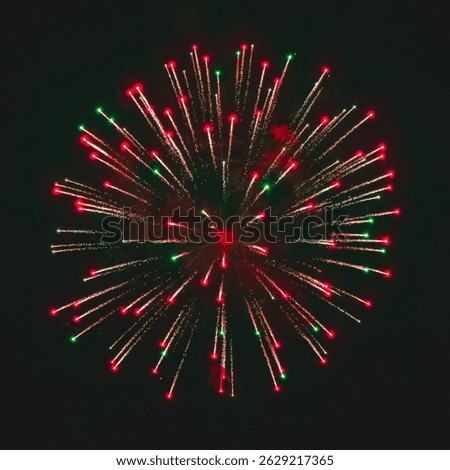 A vivid red and green firework explodes against the night sky, creating a vibrant burst of color and light. The glowing trails radiate outward, symbolizing celebration, energy, and festive spirit.