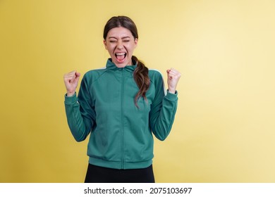 Vivid winner emotions. Portrait of young excited girl in green tracksuit posing isolated on yellow studio background in neon light. Concept of emotions, trend, style, facial expression, youth
