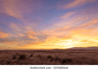 Vivid yellow sunrise over dry grassy plains with distant mountains at sunrise - Shutterstock ID 2191003161