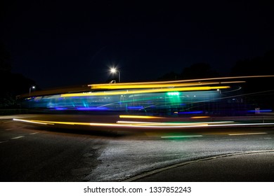 Vividly Colorful Bus Passes On An Empty Suburban Street At Night As A Ray Of Light Due To Long Exposure