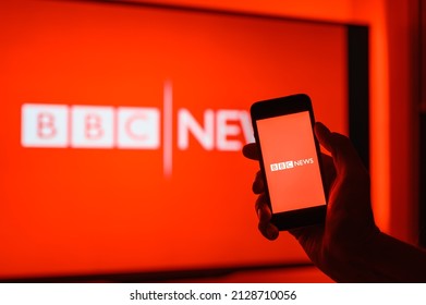 Vladimir, Russia - February 2022: Smartphone in hand with BBS application for viewing world news on the background of the BBC channel. Selective focus on the logo.