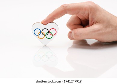 Vladimir, Russia - January 2021: Flag Of The Olympic Games. A Man's Hand Holds A Heart In The Shape Of The Olympic Flag On A White Glass Surface.