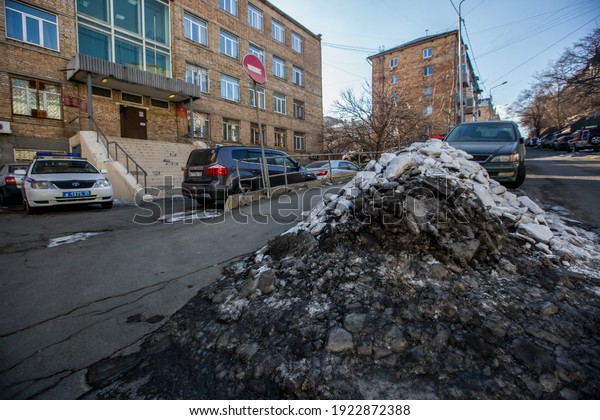 Vladivostok, Russia, 2017 - Dirty street in\
Vladivostok. Cars are parked in front of large muddy snow drifts on\
the streets of\
Vladivostok