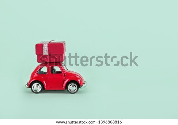 VLASOTINCE,\
SERBIA- MARCH 11, 2019: Red retro toy car with gift box on\
turquoise background. Gifts delivery concept. Valentine\'s day,\
Birthday, New Year, Mother\'s day,\
engagement.