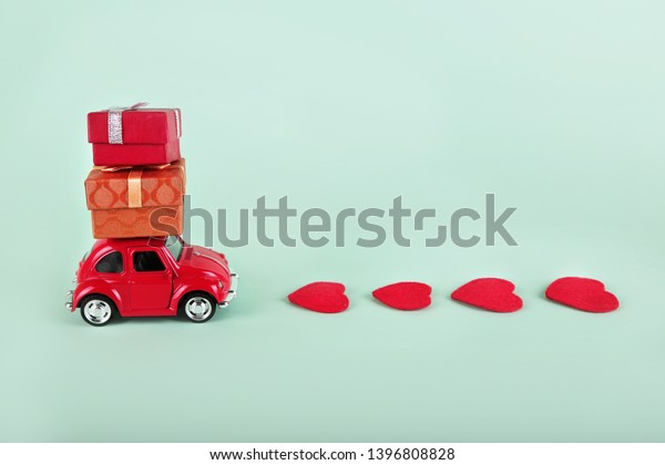 VLASOTINCE,\
SERBIA- MARCH 11, 2019: Red retro toy car with gift box and hearts\
on turquoise background. Gifts delivery concept. Valentine\'s day,\
Birthday, New Year, Mother\'s day,\
engagement.
