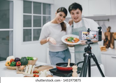 Vlogger And Blogger Freelance Job Concept, Young Asian Couple Cooking Together And Recording Live Video For Her Vlog And Social Media With Mobile Phone Camera And Tripod