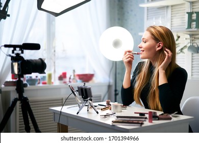 Vlogger female applies lipstick on lips. Beauty blogger woman filming daily make-up routine tutorial at camera on tripod. Influencer blonde girl live streaming cosmetics product review in home studio - Powered by Shutterstock