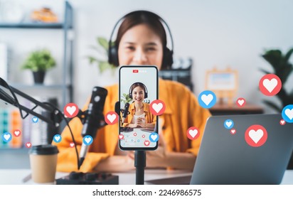 Vlogger live streaming podcast review on social media, Young Asian woman use microphones wear headphones with laptop record video. Content creator concept.