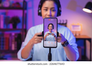 Vlogger live streaming podcast review on social media, Young Asian woman use microphones wear headphones with smartphone record video. Content creator concept.
