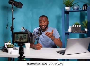 Vlogger talking with audience in excitement in front of recording digital video camera during online live show. Exalted content creator in studio looking at dslr live video podcast setup gesturing.