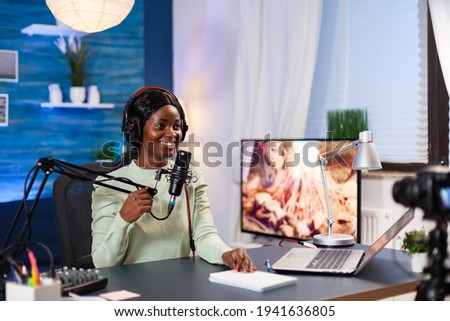 Vlogger talking with her audience while making online show from living room. Speaking during livestreaming, blogger discussing in podcast wearing headphones.