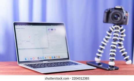 Vlogger Workplace. Laptop, Smartphone And SLR Camera On A Wooden Table. Camera On A Mini Tripod For Vlogging. Video Blogging Concept