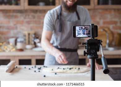 vlogging and freelance job concept. food blogger preparing blueberry pie. cooking and culinary skills concept. bearded man shooting video of himself using camera on tripod.