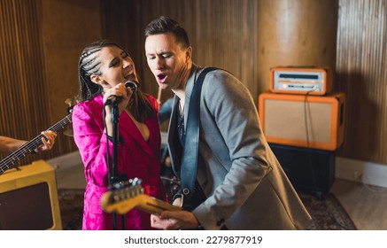 Vocalist and guitarist. Indoor portrait of caucasian woman singer singing to the microphone with male guitarist during a concert. High quality photo - Powered by Shutterstock