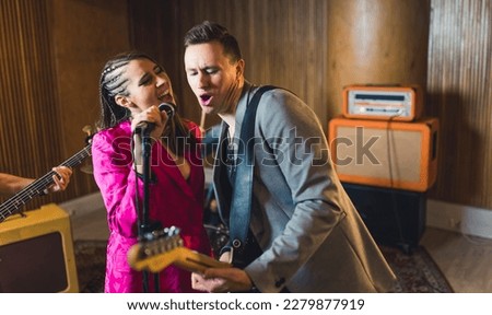 Vocalist and guitarist. Indoor portrait of caucasian woman singer singing to the microphone with male guitarist during a concert. High quality photo