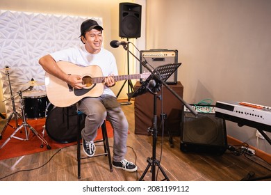 a vocalist sings while playing an acoustic guitar with musical instruments in the background