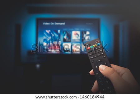 VOD service screen. Man watching TV with remote control in hand.