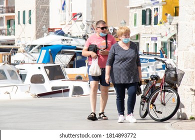 Vodice, Croatia - September 1, 2020: Overweight Mature Couple Wearing Face Surgical Masks Walking On The Promenade Dock Of  A Small Mediterranean Town By The Sea