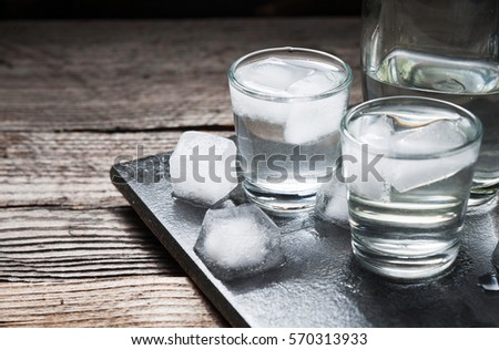 Vodka with ice in shot glasses on rustic wood background