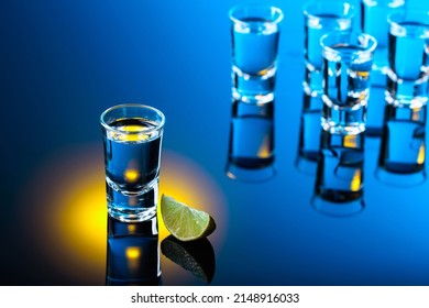 Vodka with lime slice on a black reflective background. Strong alcoholic drink in color bright lights.