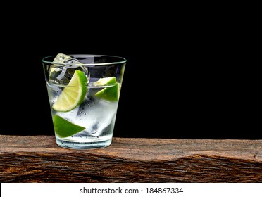 Vodka, Lime Wedge With Ice In Rocks Glass On Log With Black Background