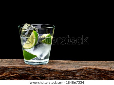 Vodka, lime wedge with ice in rocks glass on log with black background