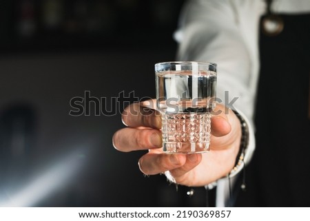 Vodka shot. Glass shot of alcohol. Bartender holds a glass shot with liquid. The trend drinks concept. Vertical photo