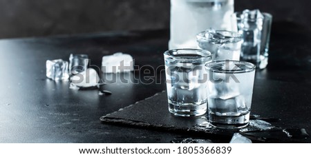 Vodka in shot glasses on black stone background, iced strong drink in misted glass