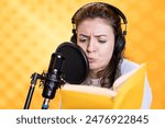 Voice actor with frown on face reading book, recording audiobook using microphone and headset, studio background. Woman using mic to produce digital recording of novel, glowering for dramatic effect