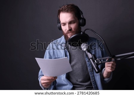 Voice actor with headphones and script performing on black background, space for text