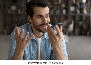 Voice application. Happy millennial male hold mobile phone talk using digital voice recorder dictate voicemail audio message. Young man enjoy tech innovation search data at web via mobile ai assistant - Powered by Shutterstock