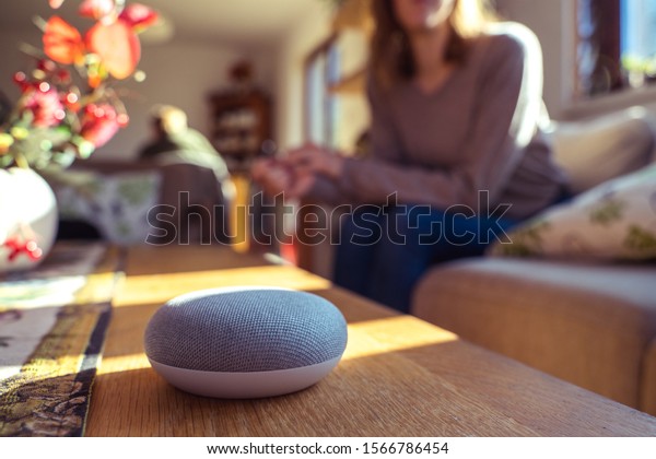 voice controlled smart speaker with a woman in the\
background in a interior home environment. Smart AI speaker concept\
