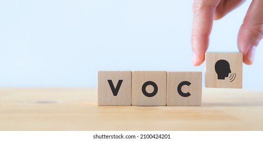 Voice of customer concept.  Consumer feedback, marketing communication. Improve and develop product, service. Customer centric. Hand holds wooden cubes with "VOC" icon on grey background ,copy space.