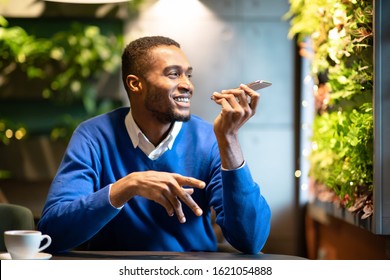 Voice Search. Happy black man using voice assistant on mobile phone or calling on smartphone at cafe, copyspace - Powered by Shutterstock