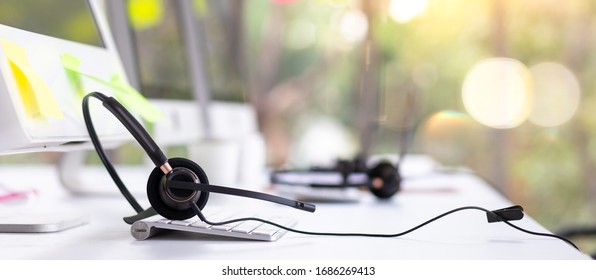  VOIP headset on desk with computer desktop at customer service and marketing support workplace. Office supplies of customer service. Communication support, call center and helpline concept.