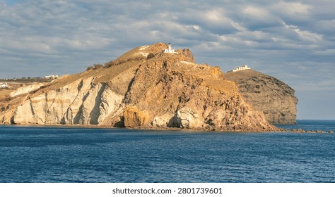 Volcanic cliffs and layered rock formations on Santorini island with a small chapel overlooking the Aegean Sea.